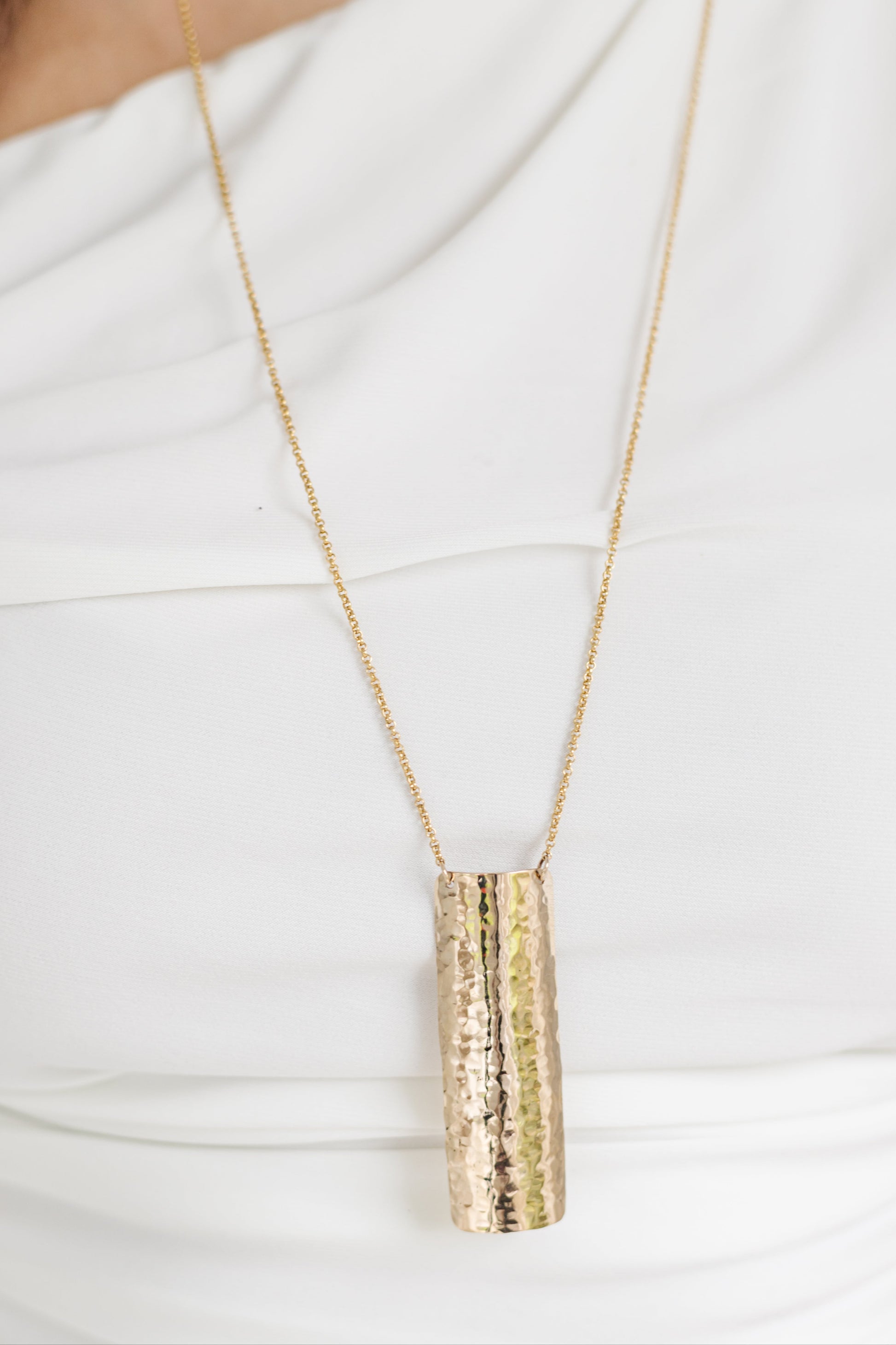 Gold necklace with a cylindrical pendant on a white background